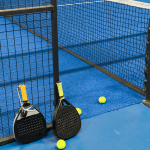 Two padel rackets on a padel blue court with several yellow balls.
